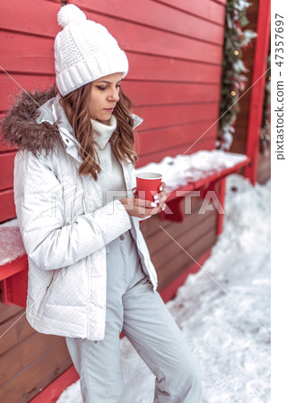 A beautiful and young girl is warming about a mug, holding cup with hot coffee or tea in her hands 47357697