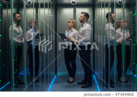 Workers in a data center walking between rows of server racks 47364908