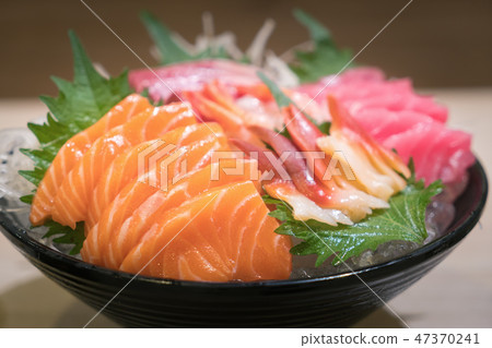 Mixed sliced fish sashimi on ice in black bowl 47370241