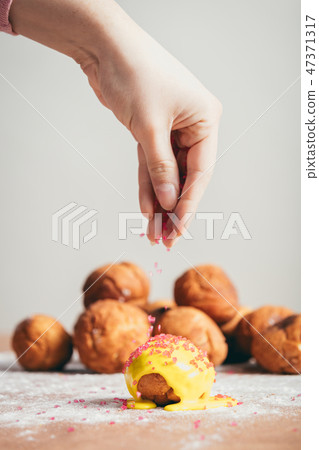 Sprinkling sugar topping on top of a doughnut. 47371317