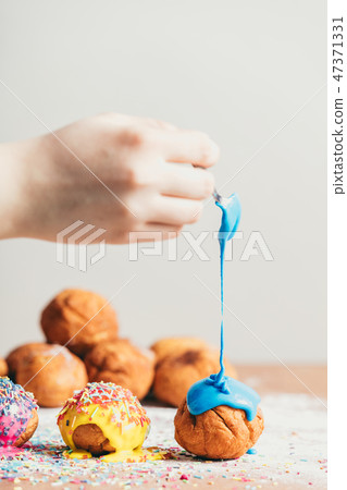 Woman's hand coating a doughnut with blue frosting. 47371331