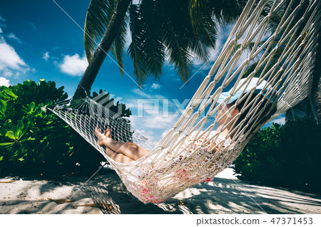 Woman relaxing in the shade of palms on a hammock. 47371453