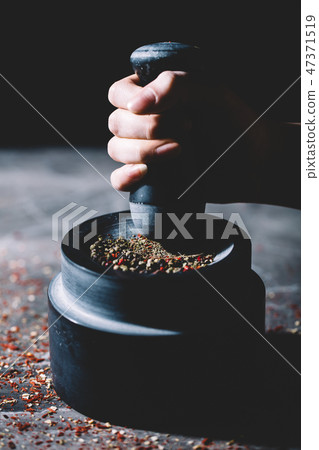 Woman's hand crushing grains of pepper in a mortar 47371519