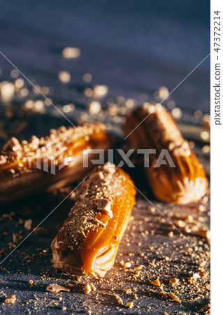 Sprinkled caramel and gold eclairs on dark background. Sprinkled caramel and gold eclairs on dark background. 47372214