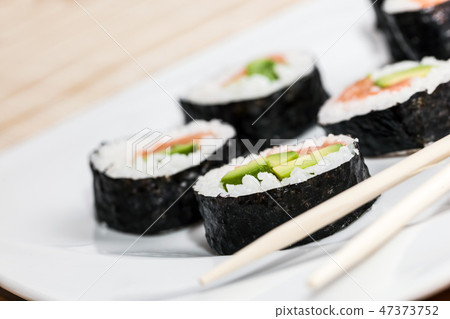 Sushi with salmon, avocado, rice in seaweed and chopsticks on a plate. 47373752