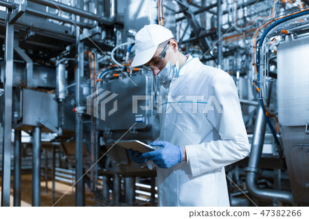 man in a mask and a Bathrobe stands with a tablet in his hands at the dairy Plant man in a mask and a Bathrobe stands with a tablet in his hands at the dairy Plant 47382266