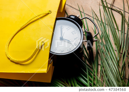 Vintage alarm clock in yellow bag and palm leaves 47384568