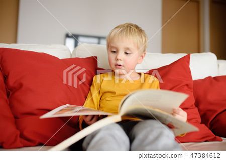 Boy is sitting at home on couch and reading book Boy is sitting at home on couch and reading book 47384612