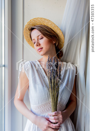 Woman in white dress holding lavender near window Woman in white dress holding lavender near window 47385355