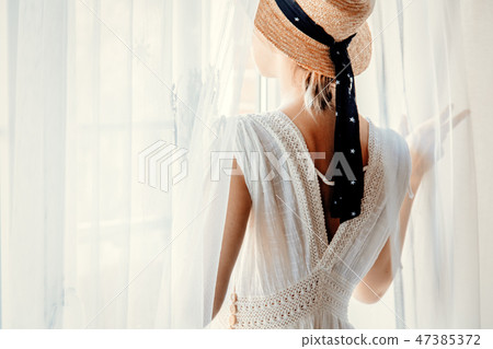 Woman in white dress holding lavender near window Woman in white dress holding lavender near window 47385372