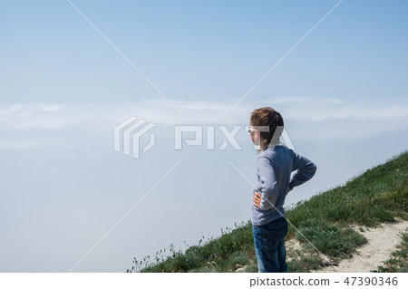 Boy stands on a mountain and looking at a thick fog. 47390346