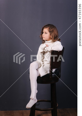 Little beautiful girl with brown hair in a white sweater. Studio. A princess poses for a Little beautiful girl with brown hair in a white sweater. Studio. A princess poses for a 47393396
