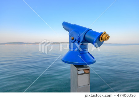 Blue public coin operated telescope, sea and island in background Blue public coin operated telescope, sea and island in background 47400356