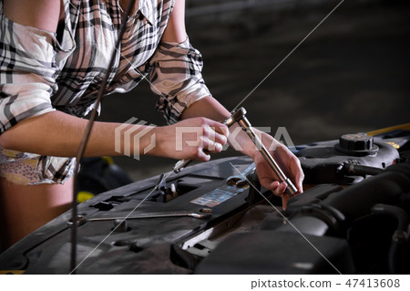 Car repair service. Young sexy woman stands in front of an opened car hood and working with a wrench 47413608