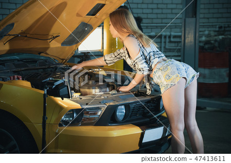 Car repair service. Young sexy woman in small shorts stands in front of an opened car hood and Car repair service. Young sexy woman in small shorts stands in front of an opened car hood and 47413611