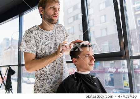 hairdresser does hair with comb of handsome satisfied client in professional hairdressing salon hairdresser does hair with comb of handsome satisfied client in professional hairdressing salon 47419410