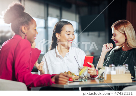 Woman holding red phone while showing her photos to friends 47422131