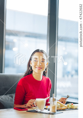Dark-eyed woman with bright lips eating and drinking coffee 47422682