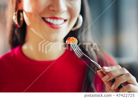 Close up of dark-haired woman eating little piece of tomato 47422725