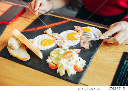 Top view of woman eating fried eggs with bacon and salad Top view of woman eating fried eggs with bacon and salad 47422745