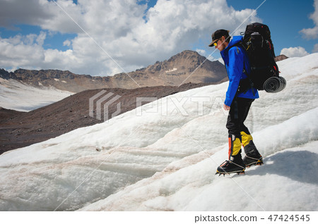 A mountaineer with a backpack walks in crampons walking along a dusty glacier with sidewalks in the 47424545