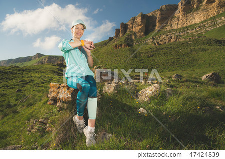 Portrait of a smiling young fitness girl in a cap and headphones checking her smart clock while Portrait of a smiling young fitness girl in a cap and headphones checking her smart clock while 47424839