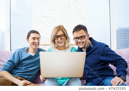 Friends sit on the couch, chatting and using a smartphone, desktop computer, laptop. 47425595