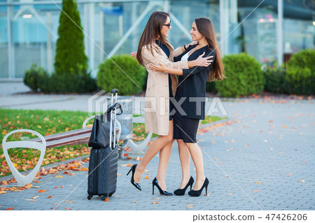 Female Friends Have a Trip Together. Front View of Cute Brunettes with Luggage at the Airport Female Friends Have a Trip Together. Front View of Cute Brunettes with Luggage at the Airport 47426206