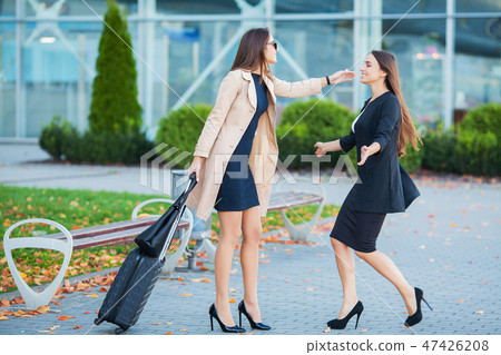 Female Friends Have a Trip Together. Front View of Cute Brunettes with Luggage at the Airport Female Friends Have a Trip Together. Front View of Cute Brunettes with Luggage at the Airport 47426208