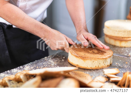 pastry chef cutting the sponge cake on layers. Cake production process. 47427137