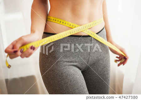 Hands measuring waist with a tape. Slim and healthy woman at her home 47427380