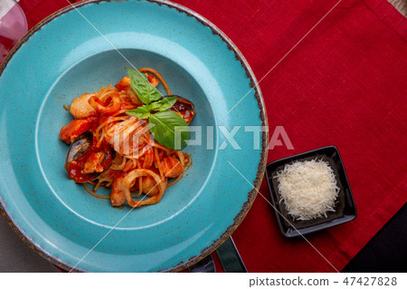 Italian cuisine. Pasta with seafood, tomatoes and cheese in a blue, a fork and a knife on a light Italian cuisine. Pasta with seafood, tomatoes and cheese in a blue, a fork and a knife on a light 47427828