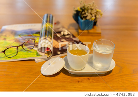 Cup of tea and glasses of water with glasses with magazine on wooden table. Cup of tea and glasses of water with glasses with magazine on wooden table. 47433098