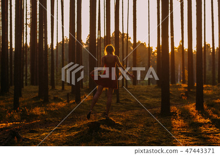 Young girl in red dress staying on the stump on one leg in fores 47443371