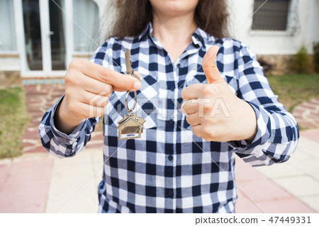 Close up of woman holding key with a keychain in the shape of the house and showing thumbs up. House Close up of woman holding key with a keychain in the shape of the house and showing thumbs up. House 47449331