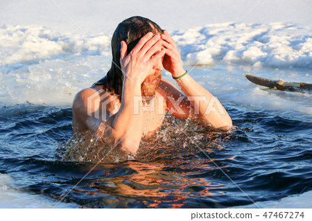 A young man is preparing to dive into the ice hole. Winter, cold, open water. 47467274