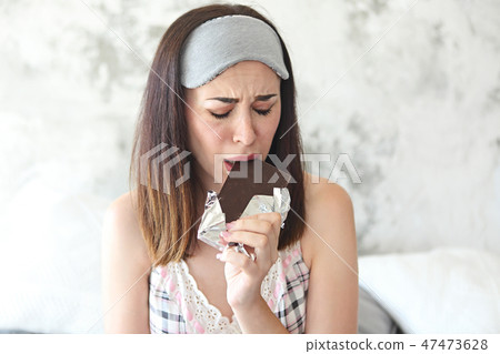 Cheerful sad young craing woman eating chocolate 47473628