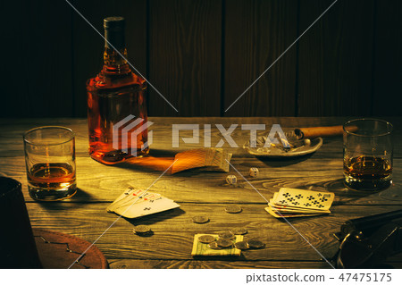 Table with playing cards, whiskey, cigar and weapons 47475175