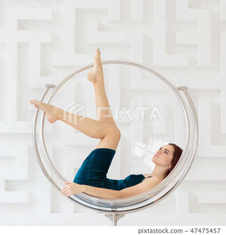Young brunette woman wearing elegant blue dress lying on round glass chair 47475457