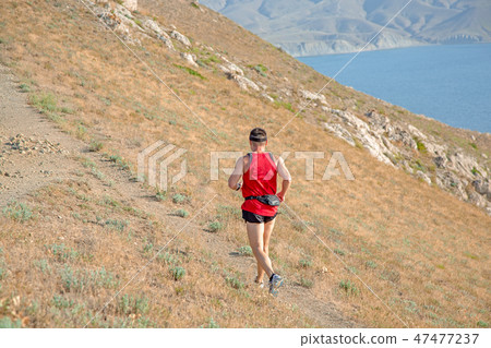 rear view of athletic runner running on a mountain trail on a blue sky background rear view of athletic runner running on a mountain trail on a blue sky background 47477237