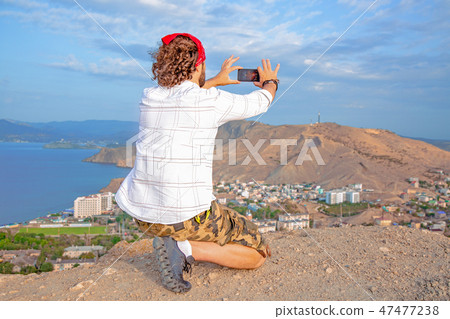 A man overlooking a panoramic view of a beautiful coastline from the hill and makes a photo on the 47477238