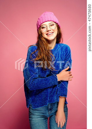 Modern young woman wearing blue sweater and pink hat posing, making funny facial expression. Modern young woman wearing blue sweater and pink hat posing, making funny facial expression. 47478680