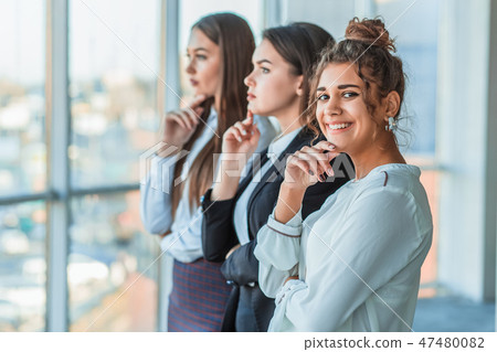 Three young beautiful brunette business ladies in the office. All serious, folded hands look to the Three young beautiful brunette business ladies in the office. All serious, folded hands look to the 47480082