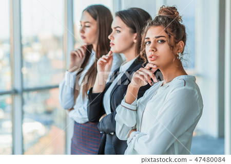 Three young beautiful brunette business ladies in the office. All serious, folded hands look to the Three young beautiful brunette business ladies in the office. All serious, folded hands look to the 47480084