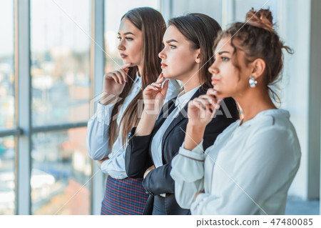 Three young beautiful brunette business ladies in the office. All serious, folded hands look to the Three young beautiful brunette business ladies in the office. All serious, folded hands look to the 47480085