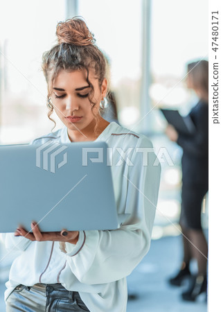 Attractive businesswoman standing on a waterfront promenade working on a laptop computer as she Attractive businesswoman standing on a waterfront promenade working on a laptop computer as she 47480171