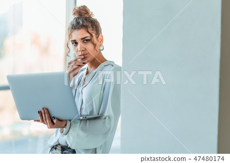 Attractive businesswoman standing on a waterfront promenade working on a laptop computer as she Attractive businesswoman standing on a waterfront promenade working on a laptop computer as she 47480174