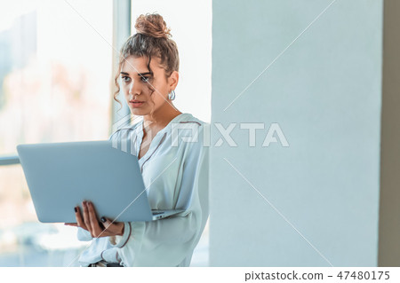 Attractive businesswoman standing on a waterfront promenade working on a laptop computer as she Attractive businesswoman standing on a waterfront promenade working on a laptop computer as she 47480175