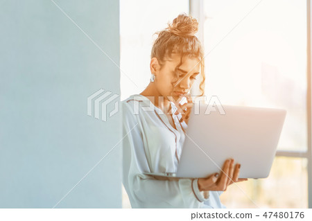 Attractive businesswoman standing on a waterfront promenade working on a laptop computer as she Attractive businesswoman standing on a waterfront promenade working on a laptop computer as she 47480176