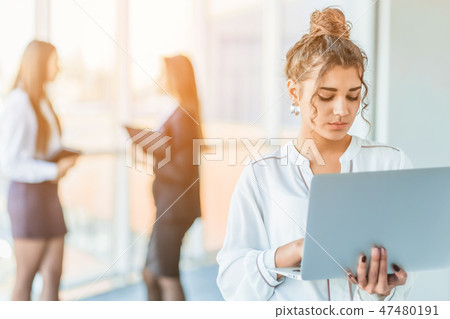 Attractive businesswoman standing on a waterfront promenade working on a laptop computer as she Attractive businesswoman standing on a waterfront promenade working on a laptop computer as she 47480191